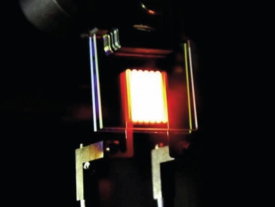 Snímek prototypu žárovky recyklující tepelné záření z laboratoří MIT. Zřetelný je nestandardní tvar vlákna poskládaného tak, aby dobře pohlcovalo tepelné záření, i „zrcadel“, která propouští viditelné světlo a odráží infračervené.